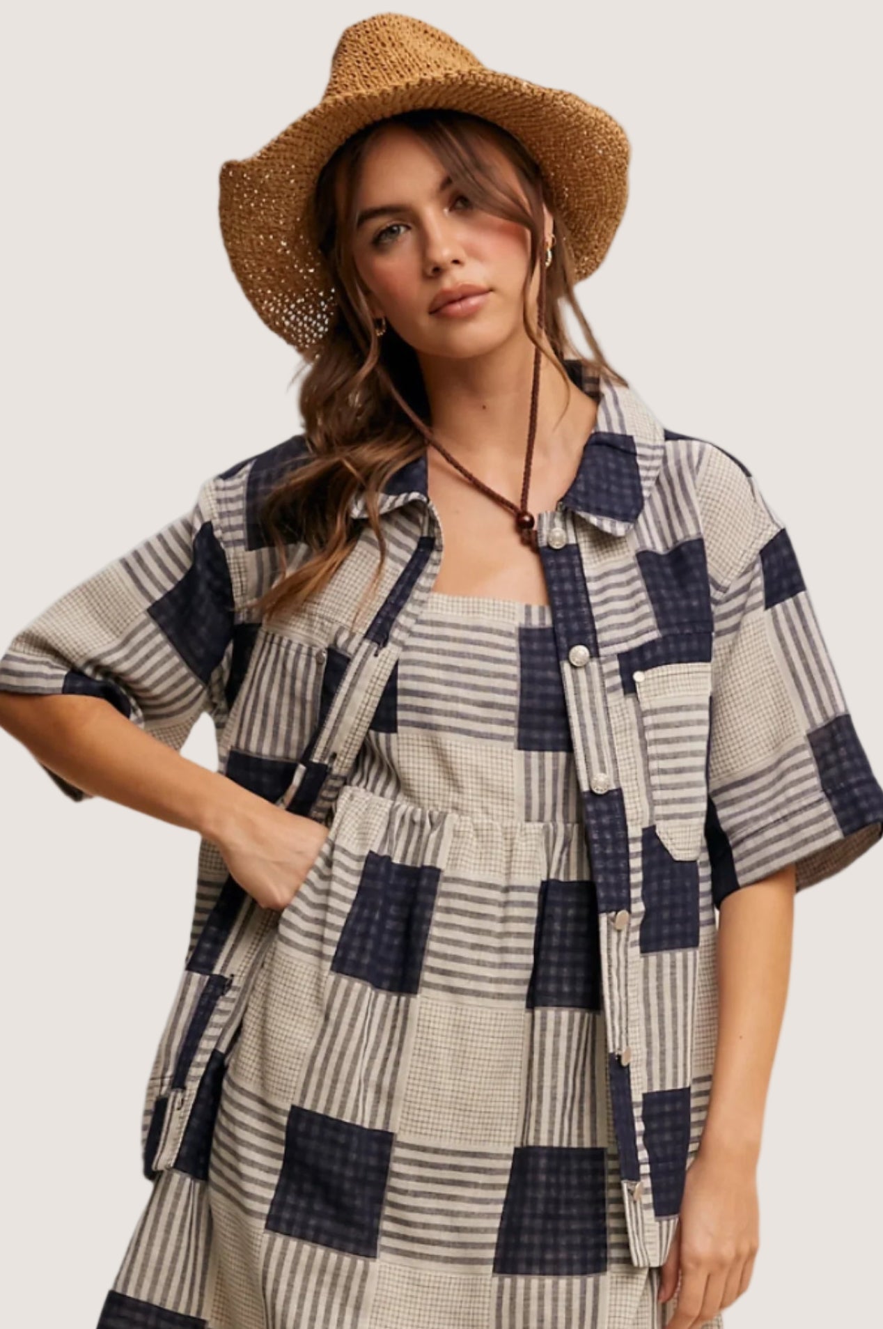 Woman wearing a checkered dress and straw hat on a beige background
